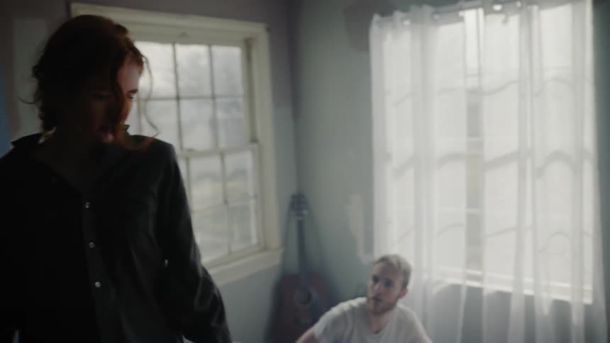 A woman gets out of bed while the man watches her from the bed