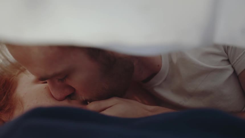 Man leans in and kisses woman under blanket