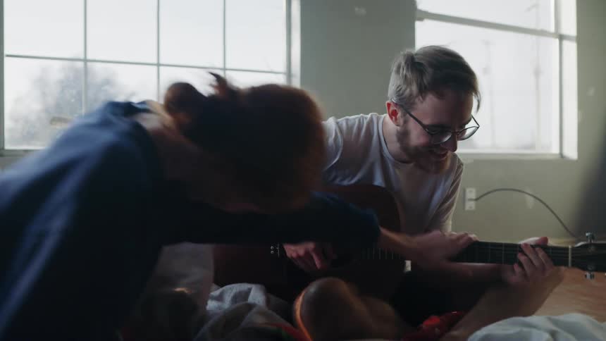 Man playing guitar while a woman laughingly stops him