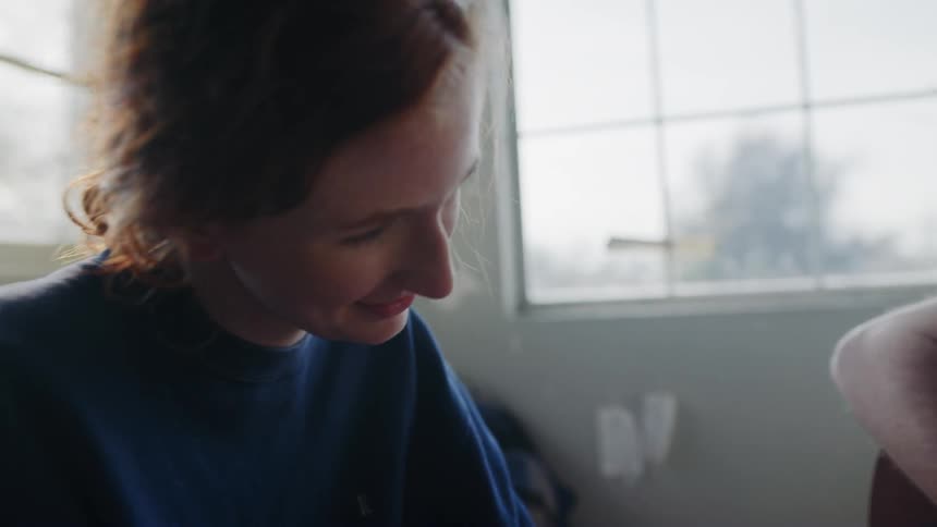 A smiling woman watching a man play a guitar