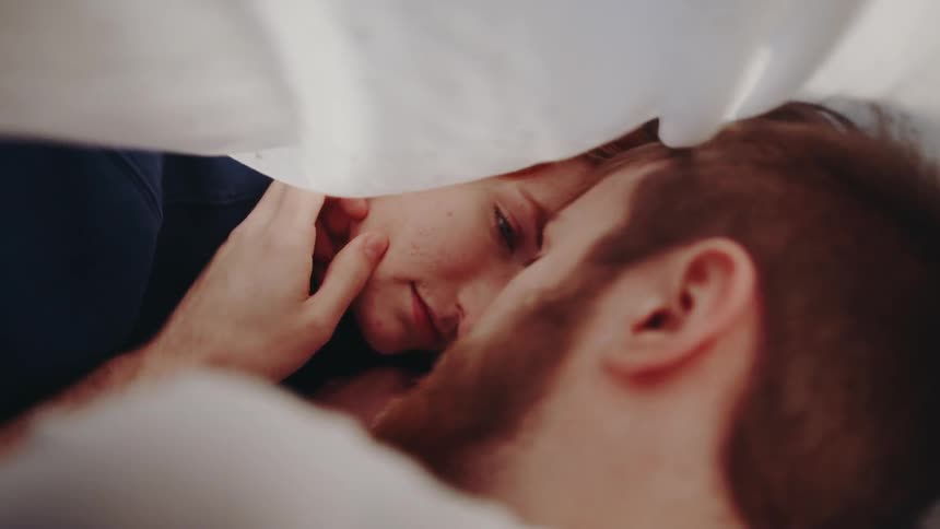 A man stroking a woman's face while they lay in bed