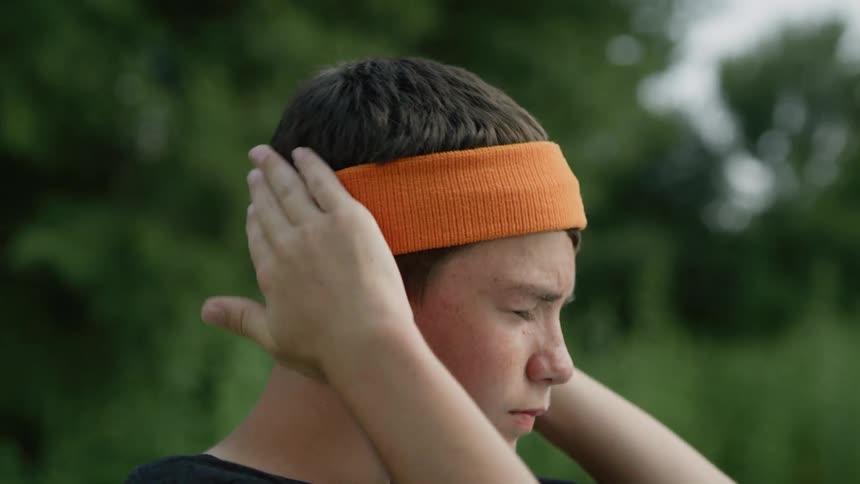 A boy putting on an orange headband standing outdoors