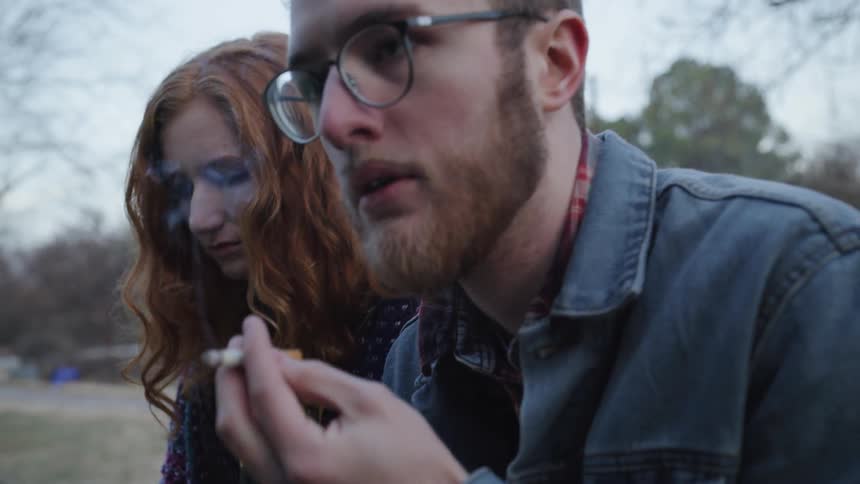 Woman passes cigarette to man while sitting outside in cold weather