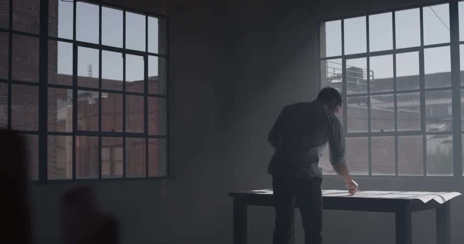 A man walks over to a table covered with papers and writes something on one of the papers