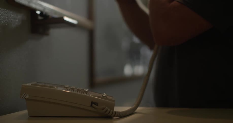 A woman lifts a phone receiver and reaches for something on a shelf