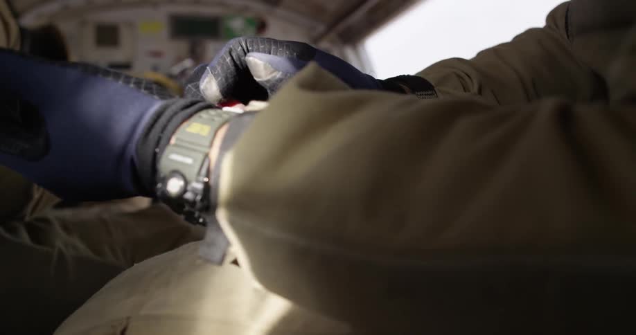 Men adjusting their gloves as the sit in an open airplane
