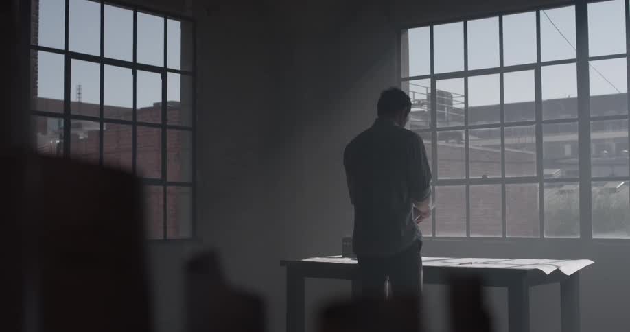 A man walking into a room and going up to a desk in front of a window
