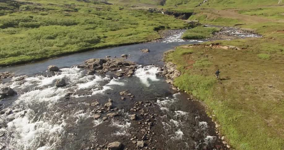 Young male running and jumping joyfully in a grassy area alongside a river