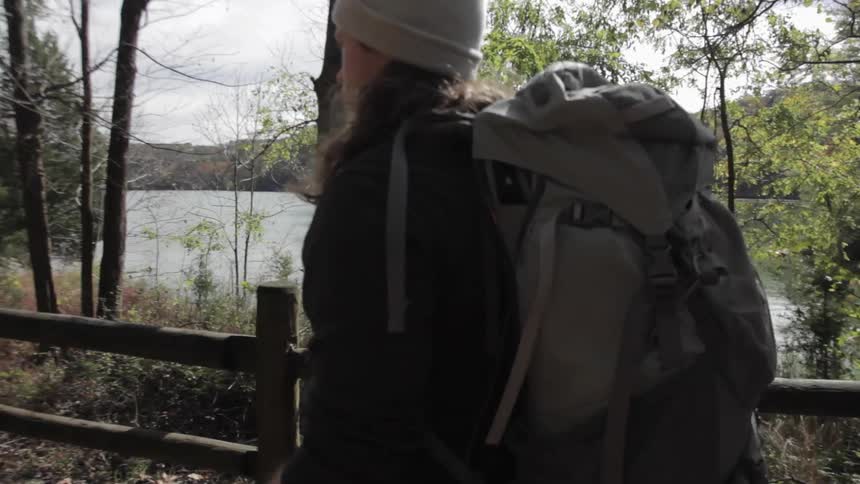 Male hiker with walking sticks and backpack walks along a lake trail