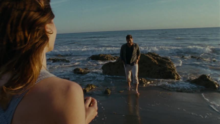 A woman taking a photo of a man standing in the surf