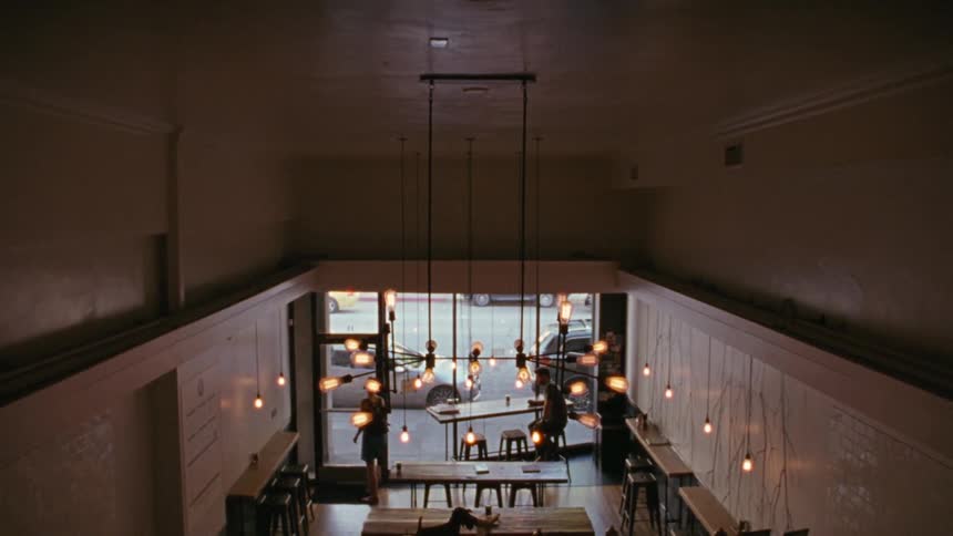 Looking down on two people sitting in a restaurant talking, and one of them gets up to leave