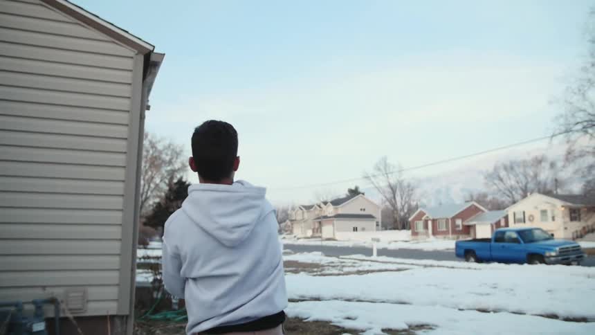 A boy throws a football to another boy who is standing on the opposite side of a snow-covered yard