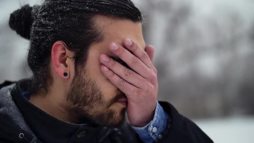 A man standing outside wipes his hand down his face as the snow falls