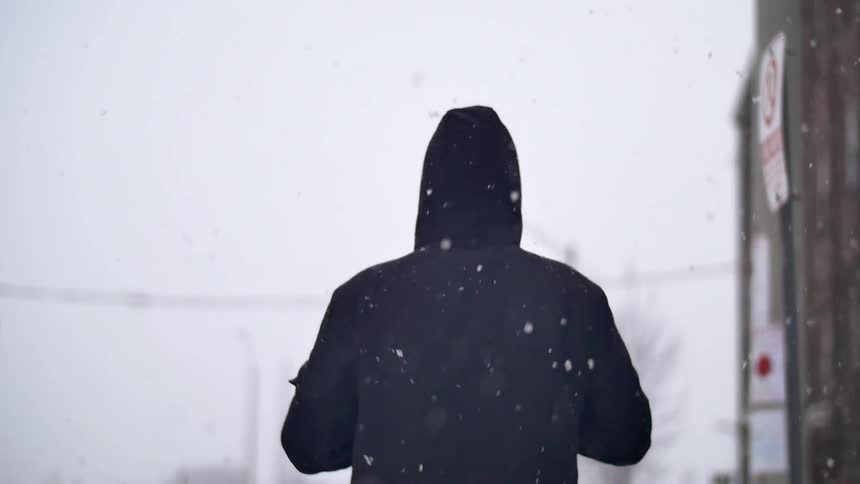 A person in a hooded coat walking while snow falls
