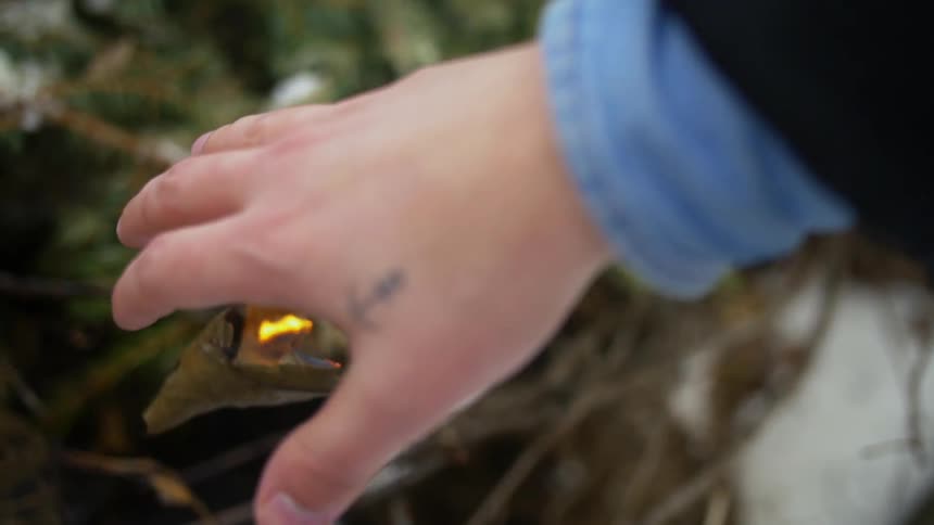 A person warming their hand over a burning leaf outside