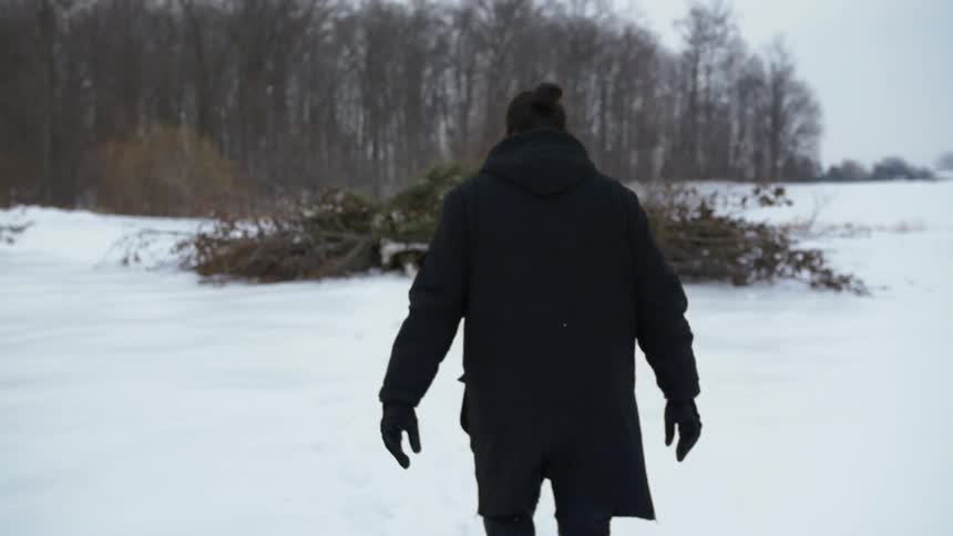 A man wearing winter clothes trudges across the snow toward some woods