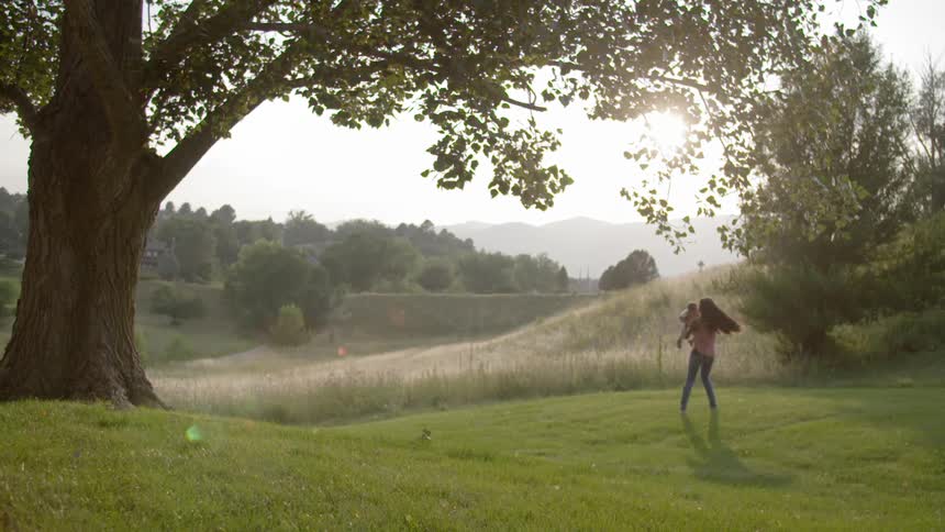 A woman swinging a baby in a grassy area