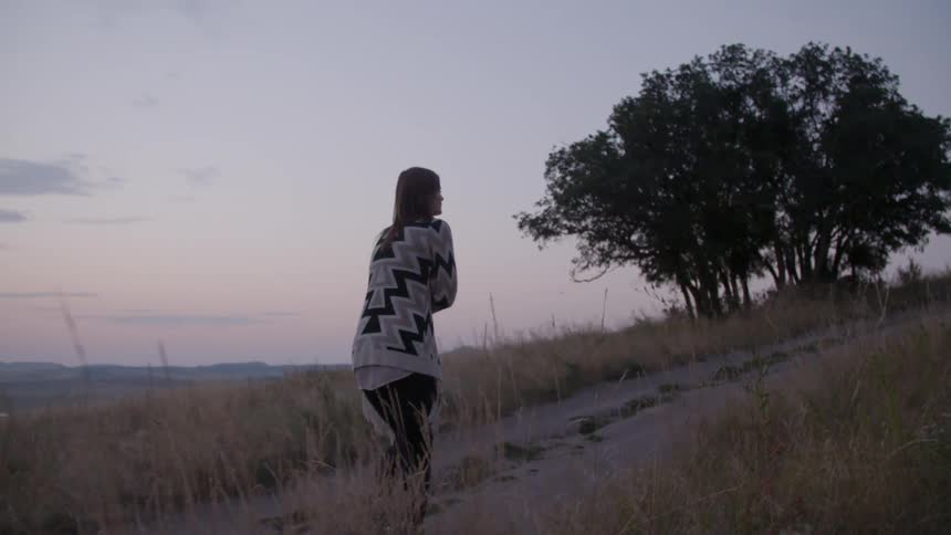 A woman wearing a sweater walking up a hill at sunset