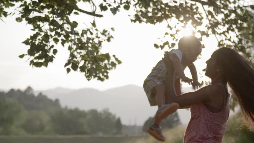A mother lifts her toddler in the air and twirls around