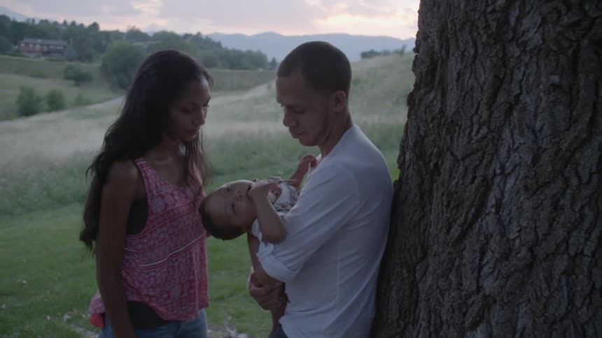 A man, a woman and a baby stand under a tree in a parklike setting