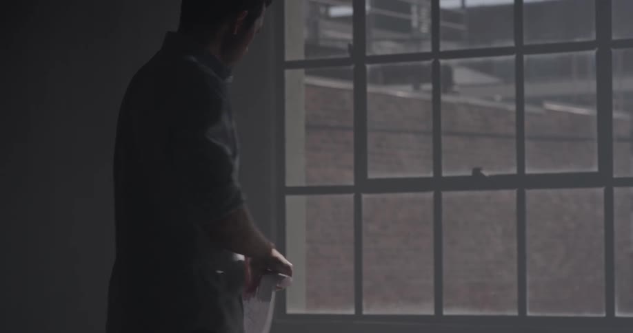 A man that is rolling up a piece of paper in front of a window