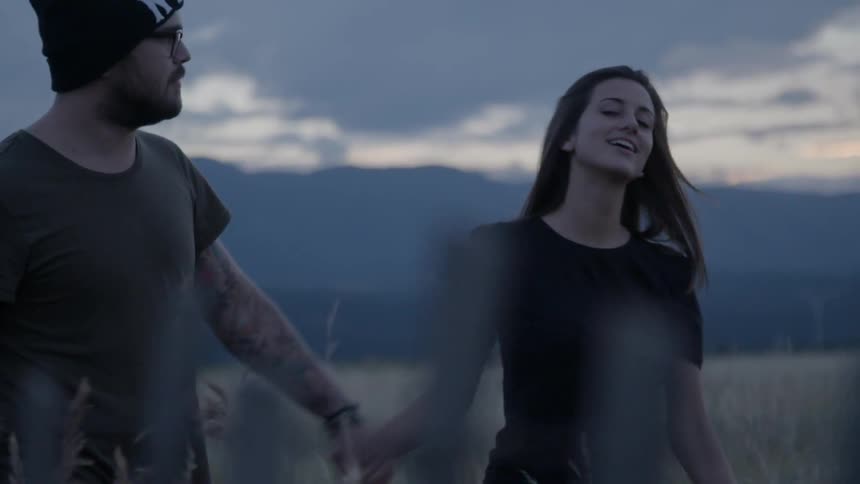 A man and woman walk through a field holding hands