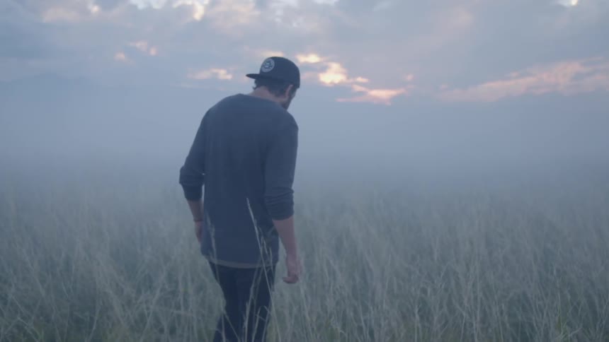 Bearded man walking through tall grass on a cloudy day