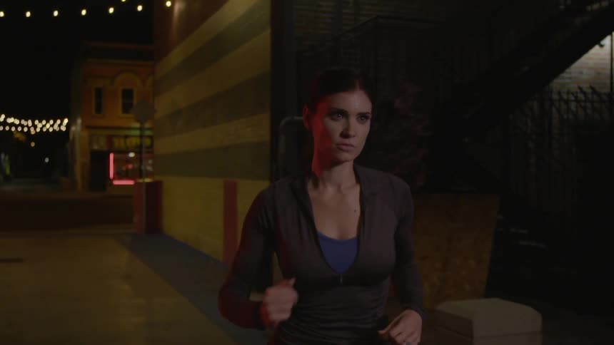 A woman jogging past storefronts at night