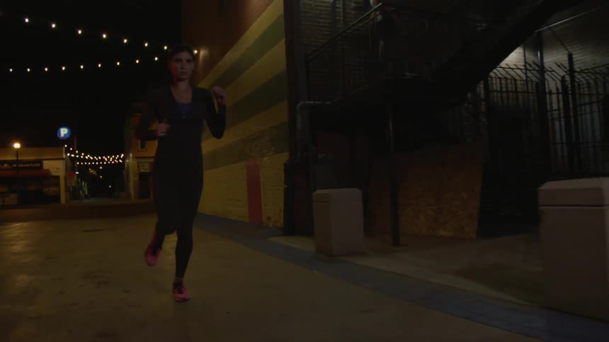 A woman jogs along an urban alley at night