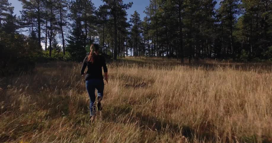 A woman is jogging outdoors through the forest
