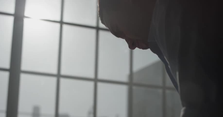 A person in a dark room is staring at the floor and takes a deep breath