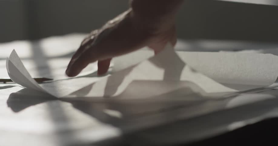 A person moves a straight edge to the paper and rips it