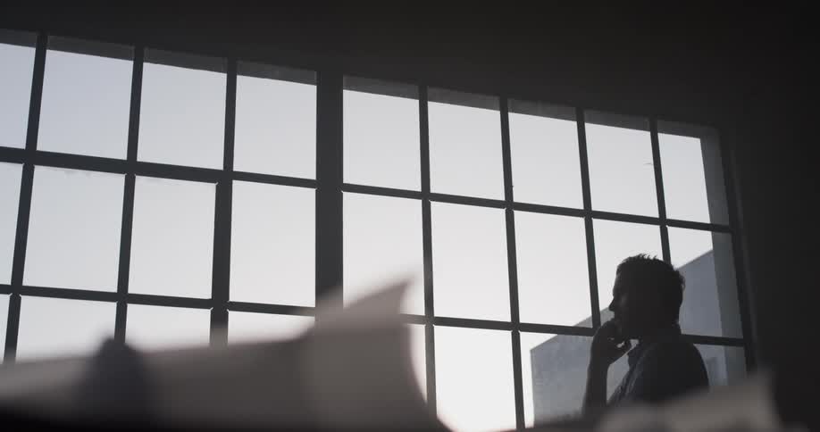 A man stands in front of windows talking on a phone