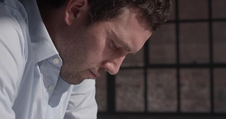 A man stares down to the floor next to the window
