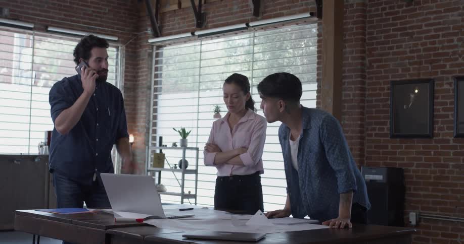 Three people stand around a table talking and looking at papers