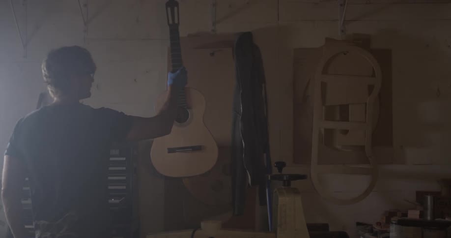 Man walking into a room and taking a guitar off the wall