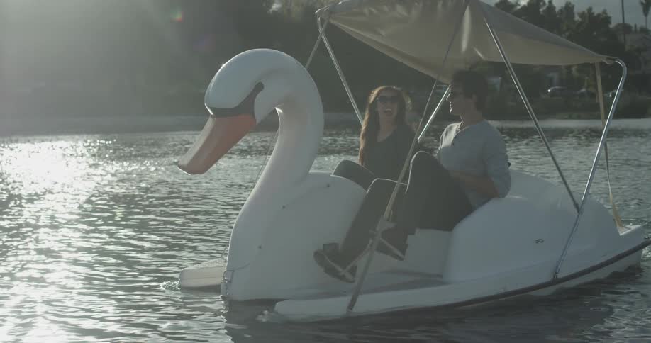 A man and woman are pedaling a swan boat