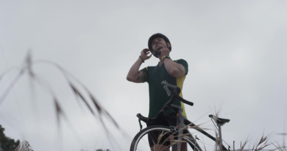 Man taking his bike helmet off while standing next to his bike in a field