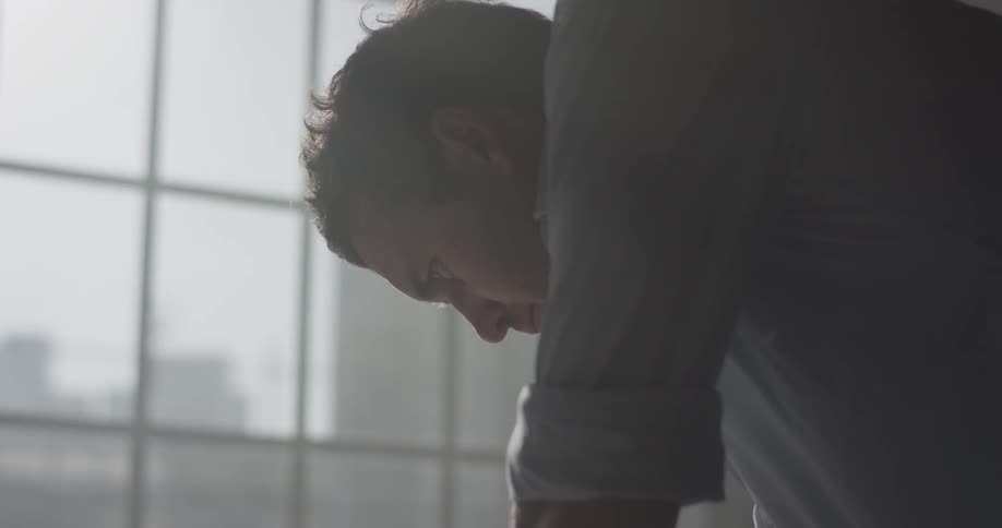 A man that is reading a piece of paper in front of a window