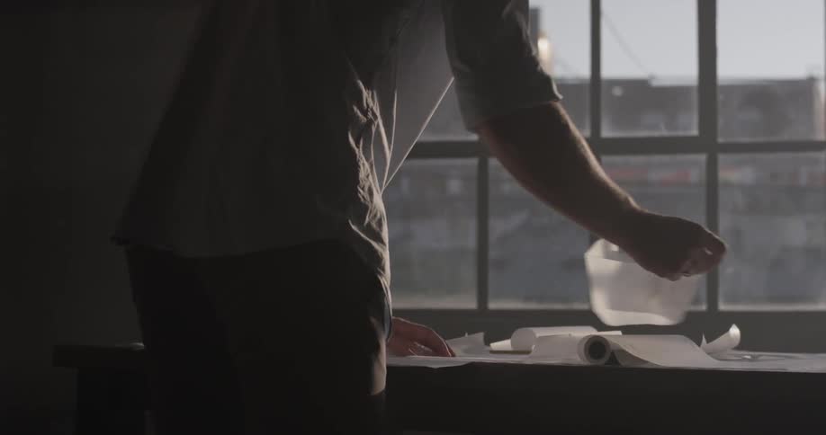 Man staring at and making notes on a paper in front of a large pane of windows