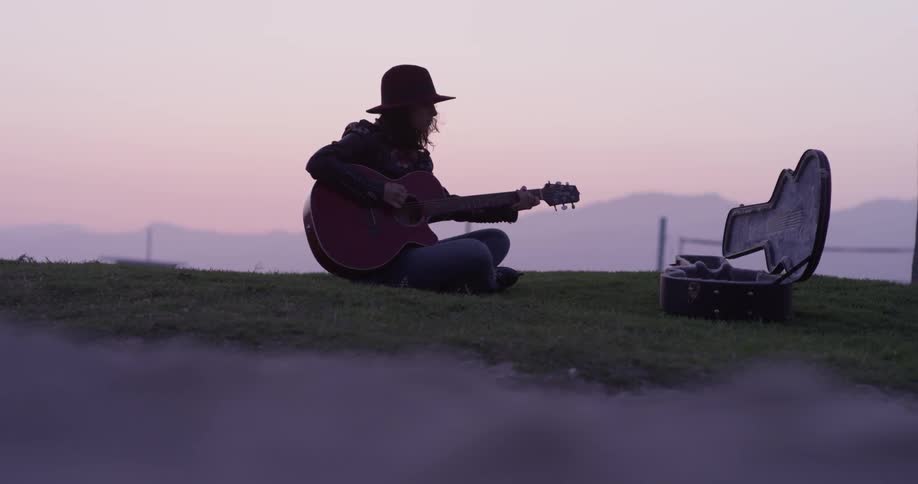 A person playing guitar sitting in the grass