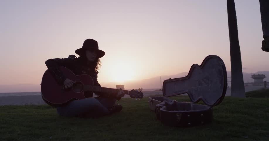 A woman plays guitar on a beach at sunset