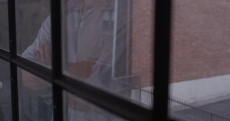 A man that is walking up to a window to look out it