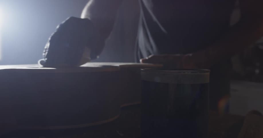 The hands of a man staining a wooden guitar