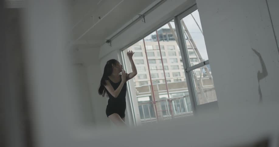 A woman dances inside a studio in the city and views her shadow on the wall