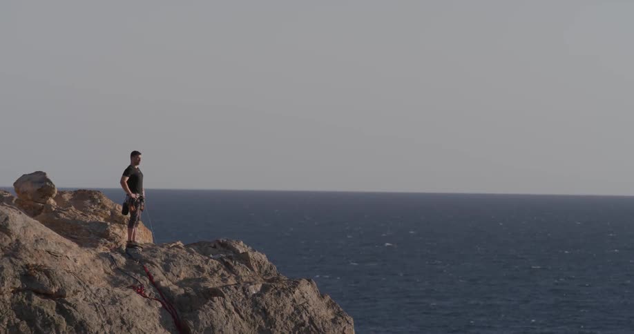 A man standing at the top of a cliff wearing a harness