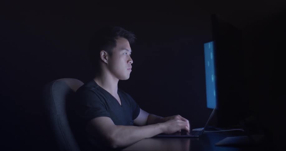 Man types on laptop while sitting at desk with a second monitor