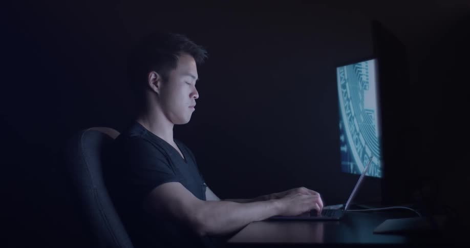 A man is sitting at a desk working on a laptop with other screens beside it