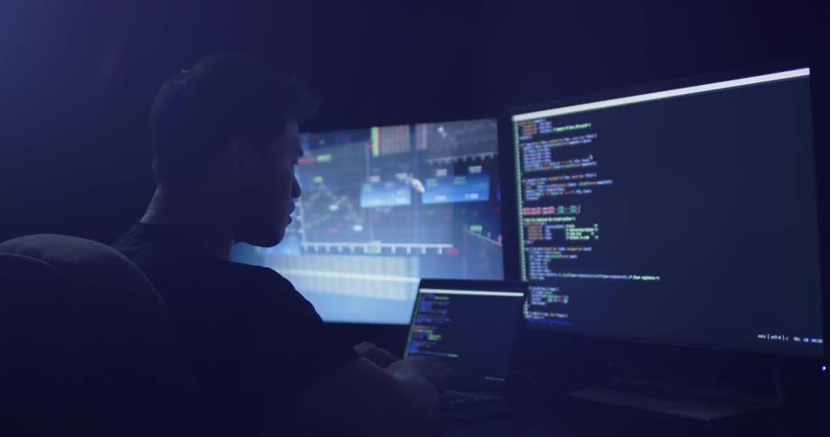 Man at desk looks with two monitors types on laptop keyboard
