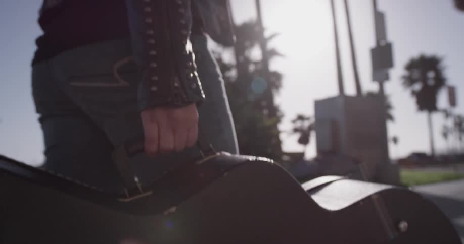 A person is walking and holding a guitar outside